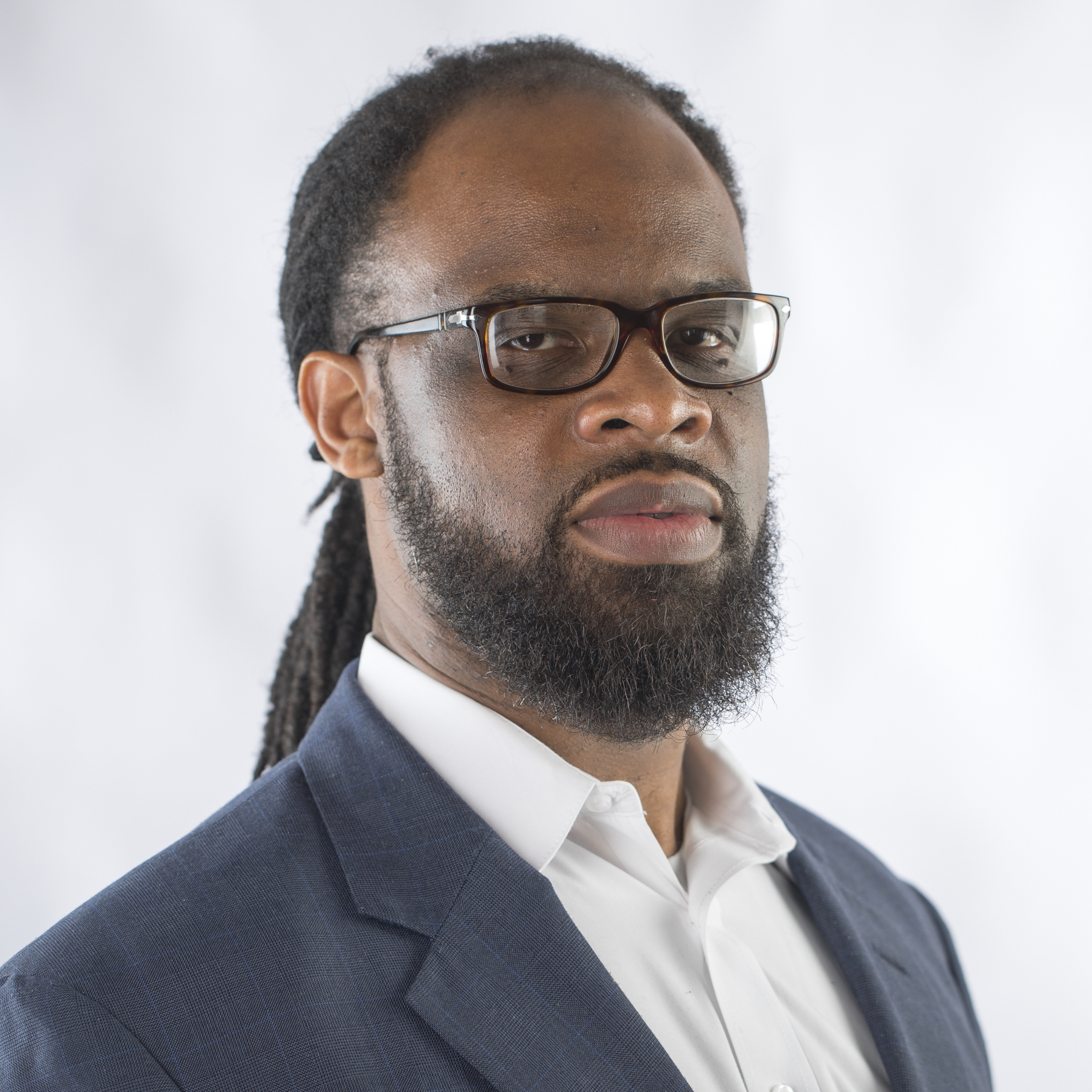 Picture of a man with long hair pulled back and a beard wearing a suit