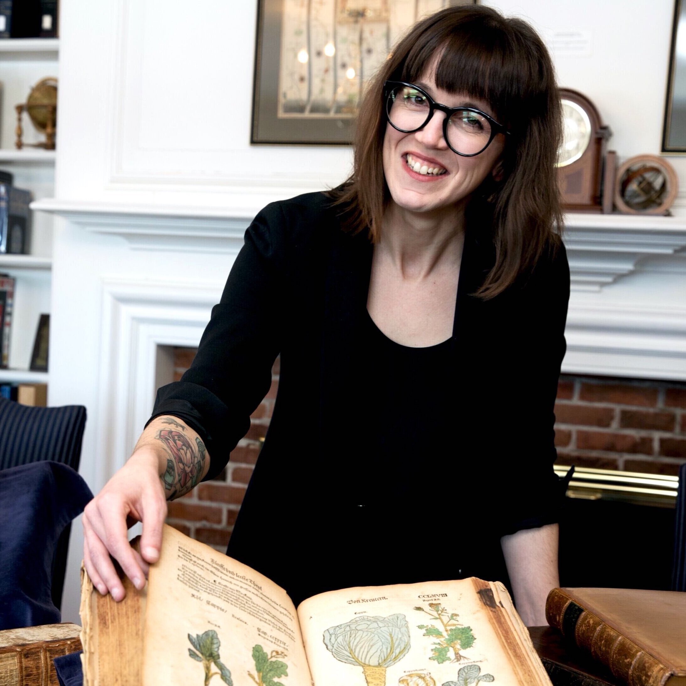 Picture of a smiling woman with long hair and glasses holding a big book