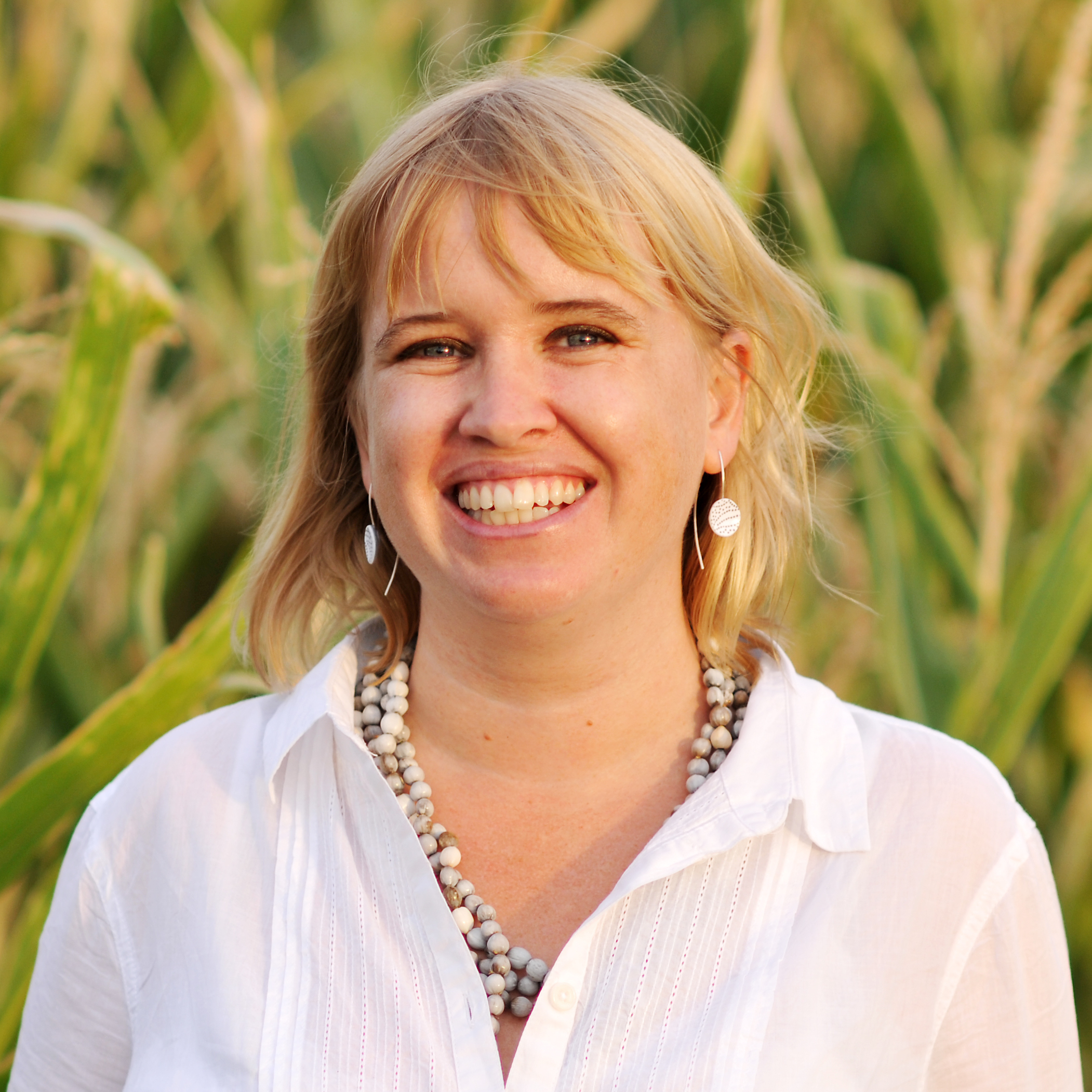 Picture of a smiling woman with shoulder-length blonde hair in front of a corn field